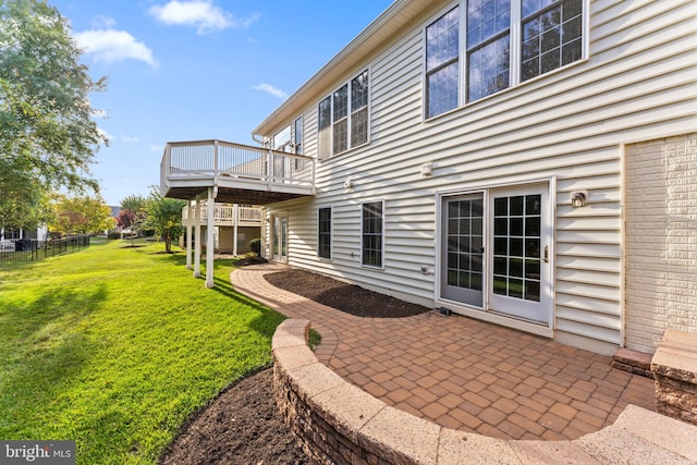 rear view of property with a wooden deck, a lawn, and a patio