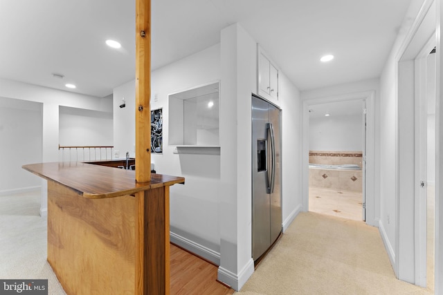 kitchen featuring white cabinetry, stainless steel refrigerator with ice dispenser, light carpet, and kitchen peninsula