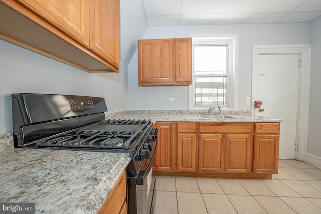 kitchen with black gas range, light stone counters, light tile patterned floors, a drop ceiling, and sink