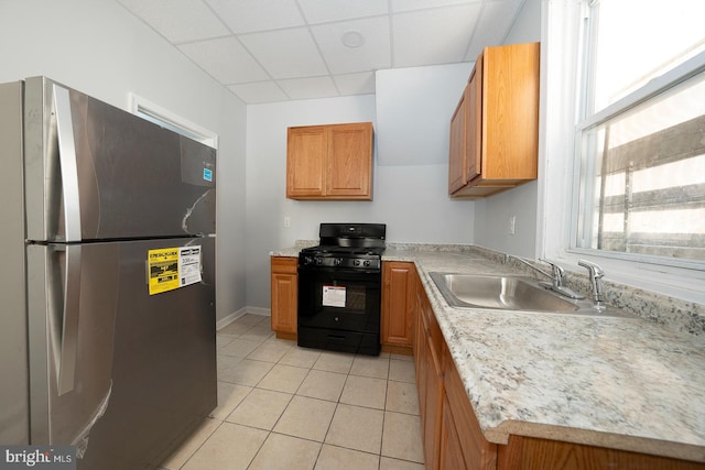 kitchen with sink, stainless steel fridge, a paneled ceiling, black range with gas cooktop, and light tile patterned floors