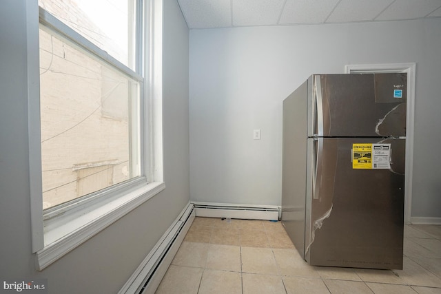 kitchen featuring stainless steel fridge, a paneled ceiling, a baseboard radiator, and light tile patterned floors