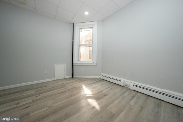 empty room featuring light hardwood / wood-style floors, a drop ceiling, and a baseboard radiator