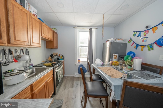 kitchen featuring light hardwood / wood-style floors, a drop ceiling, baseboard heating, and stainless steel appliances