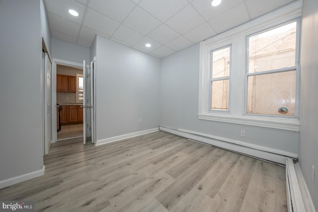 unfurnished room featuring a baseboard radiator, light hardwood / wood-style flooring, and a paneled ceiling