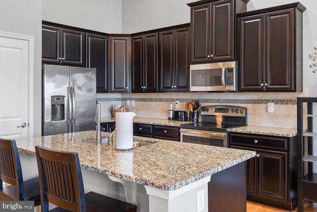 kitchen with a center island with sink, dark brown cabinets, a kitchen breakfast bar, and stainless steel appliances