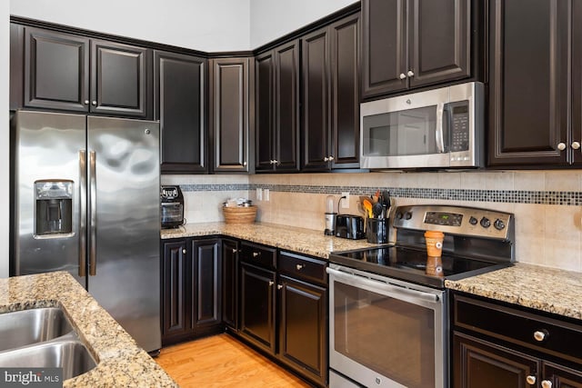 kitchen with light hardwood / wood-style flooring, stainless steel appliances, dark brown cabinetry, light stone counters, and tasteful backsplash