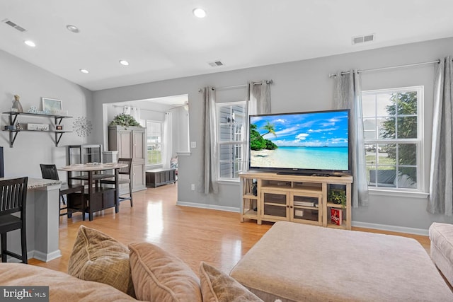 living room with light hardwood / wood-style floors, vaulted ceiling, and a wealth of natural light