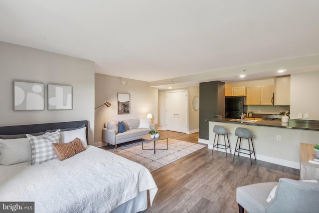 bedroom with hardwood / wood-style flooring, sink, and black refrigerator