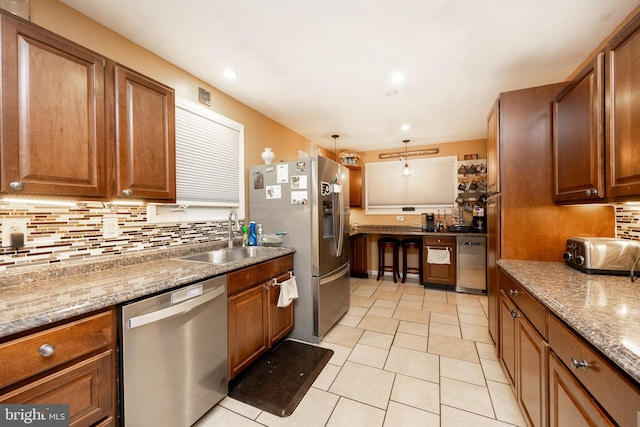 kitchen with light stone countertops, sink, decorative light fixtures, and appliances with stainless steel finishes