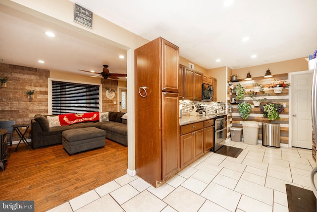 kitchen with light wood-type flooring, backsplash, light stone countertops, oven, and ceiling fan