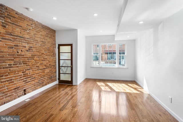 empty room with brick wall and light hardwood / wood-style flooring