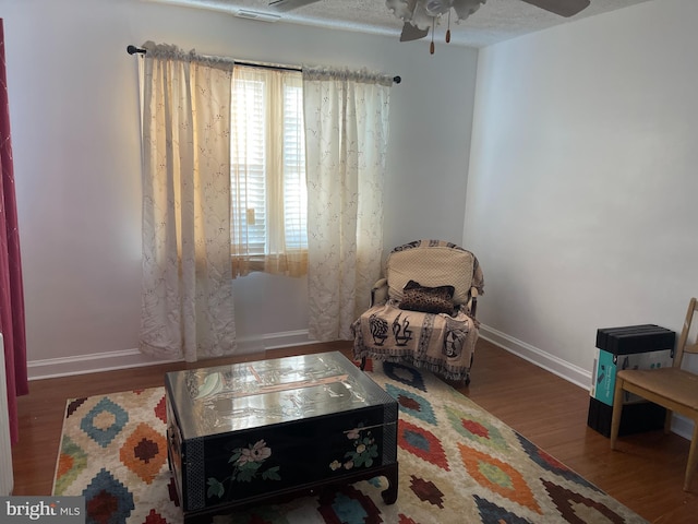 living area with a textured ceiling, dark wood-type flooring, and ceiling fan