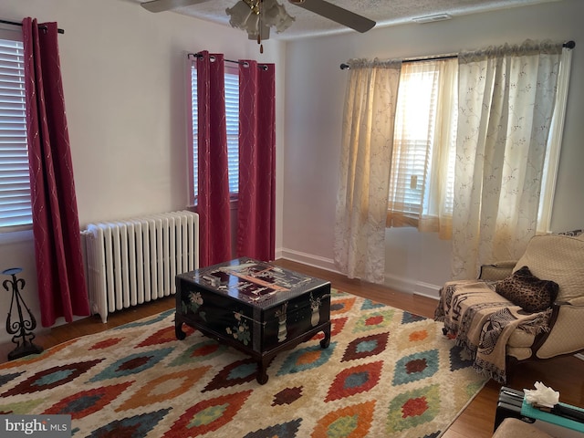 sitting room with radiator, ceiling fan, hardwood / wood-style flooring, and a textured ceiling