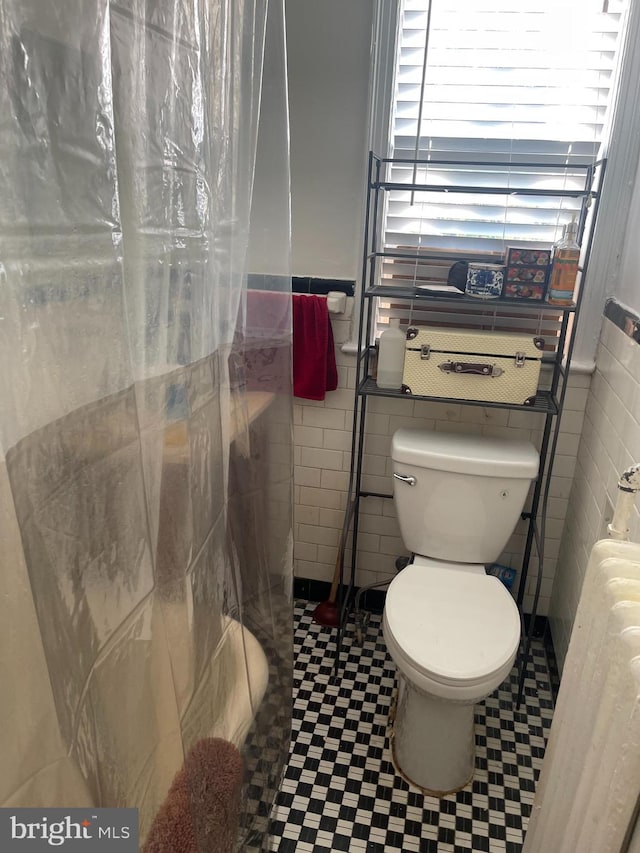 bathroom featuring toilet, a shower with curtain, and tile walls