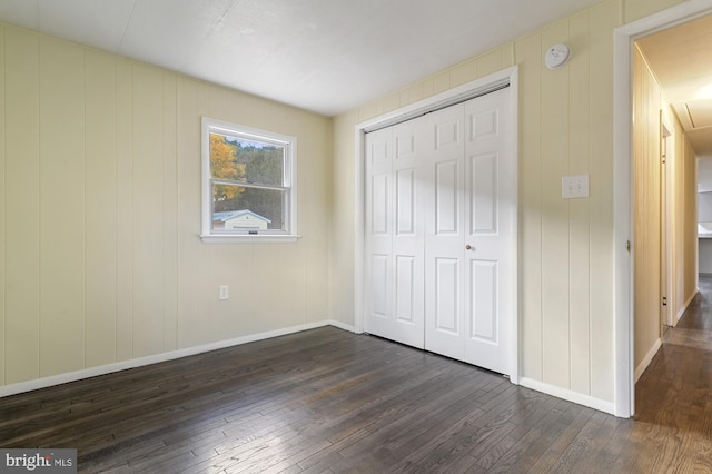 unfurnished bedroom with dark wood-type flooring, a closet, and wood walls