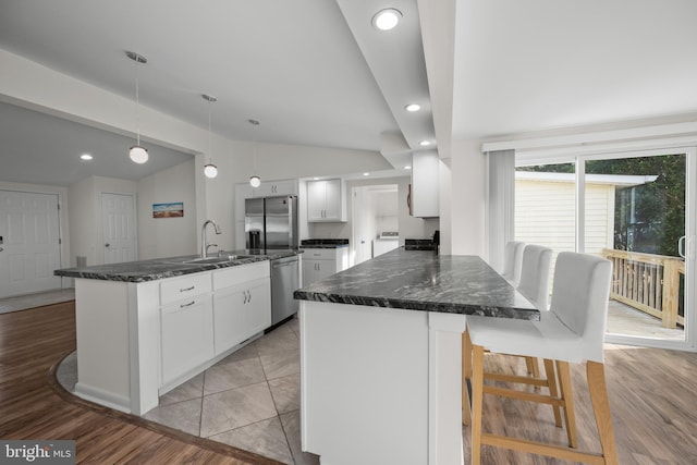 kitchen featuring appliances with stainless steel finishes, decorative light fixtures, light hardwood / wood-style flooring, white cabinets, and lofted ceiling