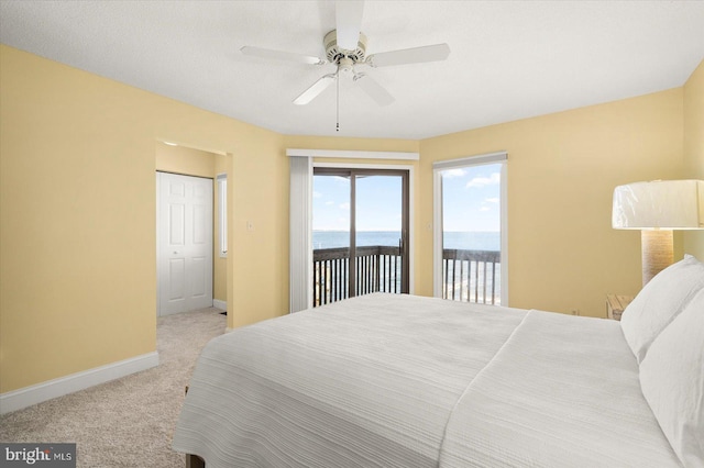 carpeted bedroom featuring access to exterior, a water view, and ceiling fan