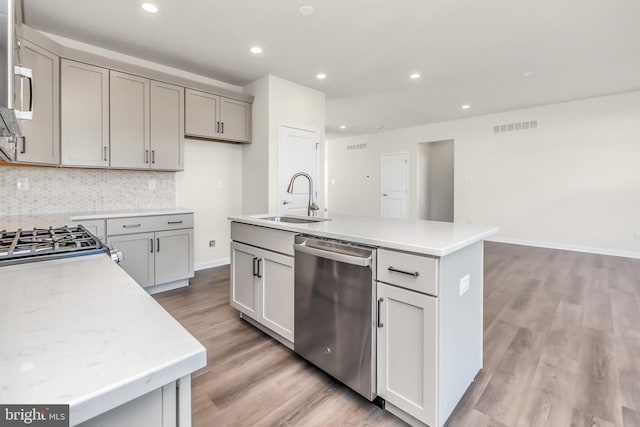 kitchen featuring stainless steel dishwasher, sink, a kitchen island with sink, and gray cabinets