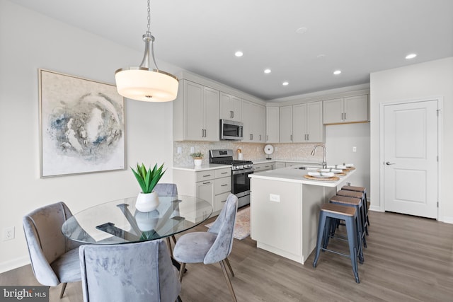 kitchen featuring appliances with stainless steel finishes, hardwood / wood-style floors, a center island with sink, and pendant lighting