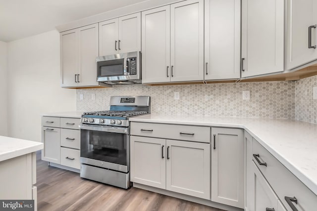 kitchen with appliances with stainless steel finishes, white cabinetry, light hardwood / wood-style floors, and tasteful backsplash