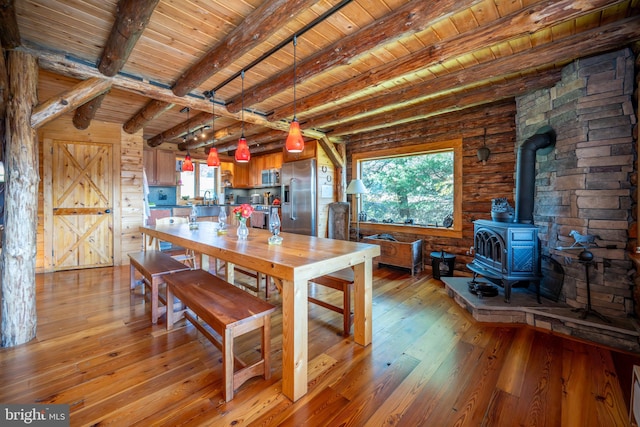 dining room with a wood stove, sink, wooden ceiling, beamed ceiling, and light hardwood / wood-style flooring