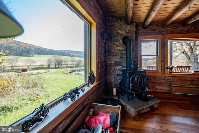 sunroom featuring wooden ceiling, beam ceiling, a rural view, a wood stove, and a mountain view