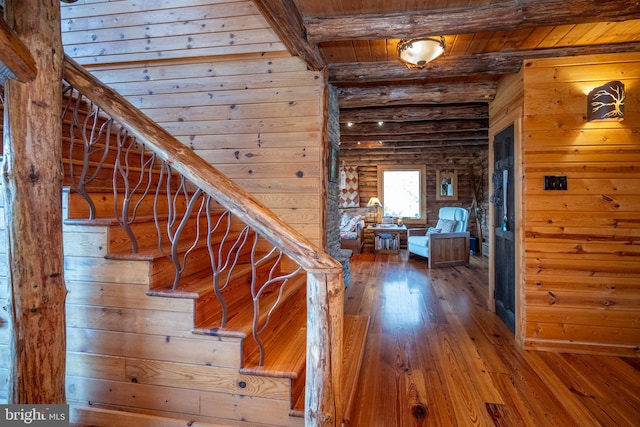 stairway with wood walls, wood-type flooring, and beam ceiling