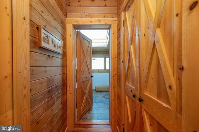 corridor featuring baseboard heating, wooden walls, and wood-type flooring