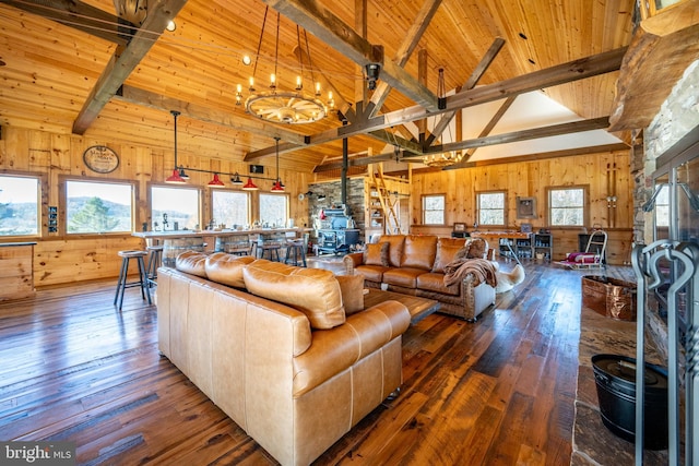 living room featuring a wood stove, beam ceiling, wooden walls, hardwood / wood-style floors, and an inviting chandelier