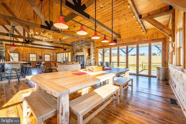 dining room featuring a stone fireplace, hardwood / wood-style floors, wood walls, and beamed ceiling