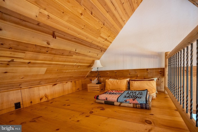 bedroom featuring light hardwood / wood-style floors, wood walls, and vaulted ceiling