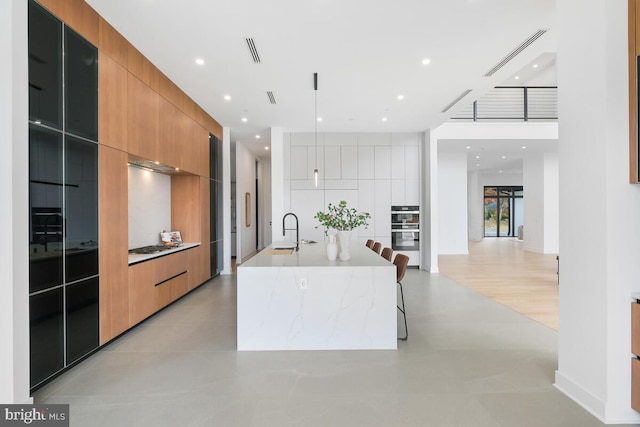 kitchen with sink, a kitchen breakfast bar, double oven, light stone countertops, and a spacious island