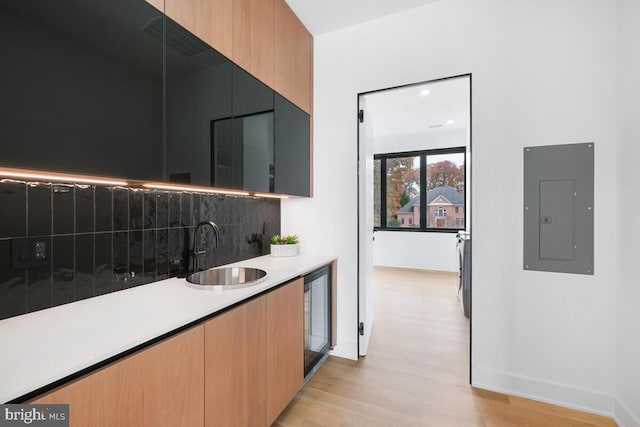 kitchen with wine cooler, sink, electric panel, light wood-type flooring, and decorative backsplash