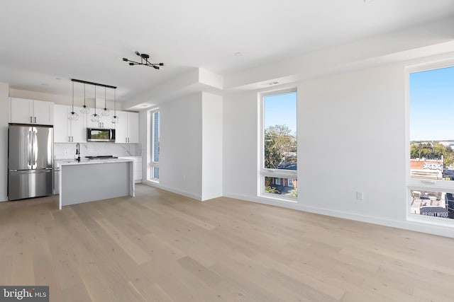 kitchen with tasteful backsplash, white cabinetry, light wood-type flooring, pendant lighting, and stainless steel appliances