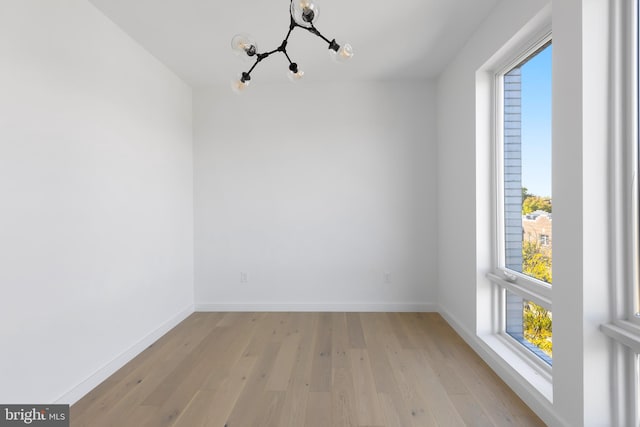 unfurnished room featuring a notable chandelier and light wood-type flooring