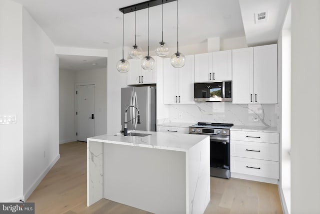 kitchen featuring an island with sink, stainless steel appliances, pendant lighting, light wood-type flooring, and white cabinets