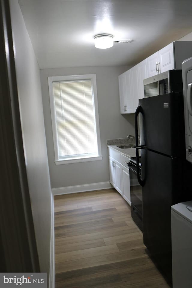 kitchen with sink, black appliances, white cabinetry, and light hardwood / wood-style flooring