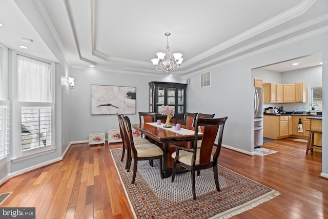 dining room featuring light wood-type flooring, plenty of natural light, and a raised ceiling