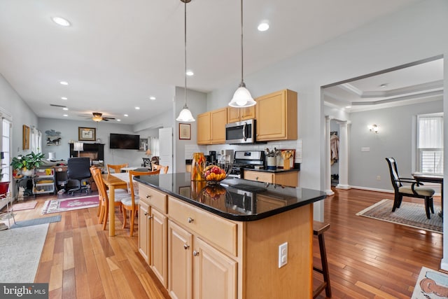 kitchen featuring a breakfast bar, appliances with stainless steel finishes, ceiling fan, a kitchen island, and light wood-type flooring