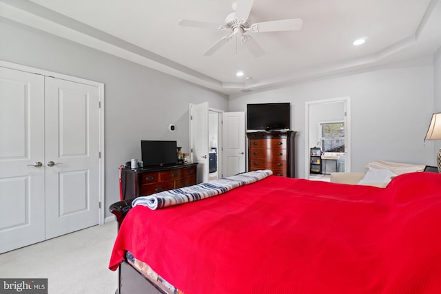 bedroom featuring ceiling fan, light colored carpet, a closet, and a tray ceiling