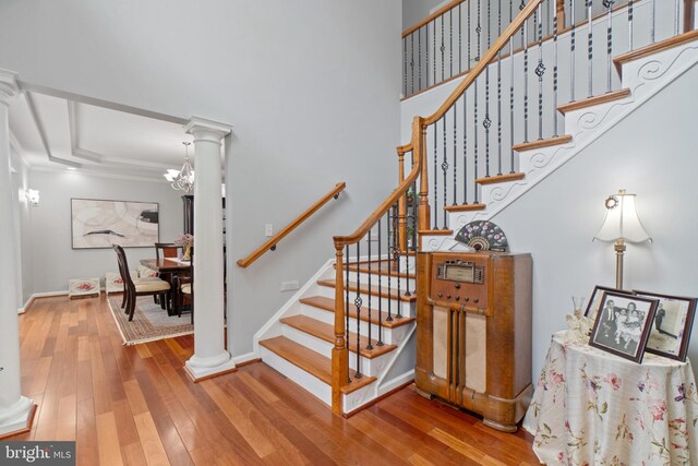 staircase with a raised ceiling, hardwood / wood-style flooring, a chandelier, and decorative columns