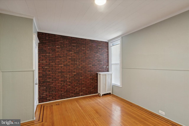 empty room featuring ornamental molding, brick wall, and light wood-type flooring