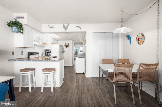 kitchen featuring white fridge, dark hardwood / wood-style flooring, hanging light fixtures, white cabinets, and kitchen peninsula