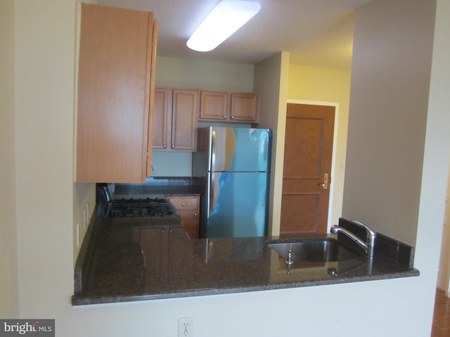 kitchen with kitchen peninsula, stainless steel fridge, black stove, dark stone counters, and sink