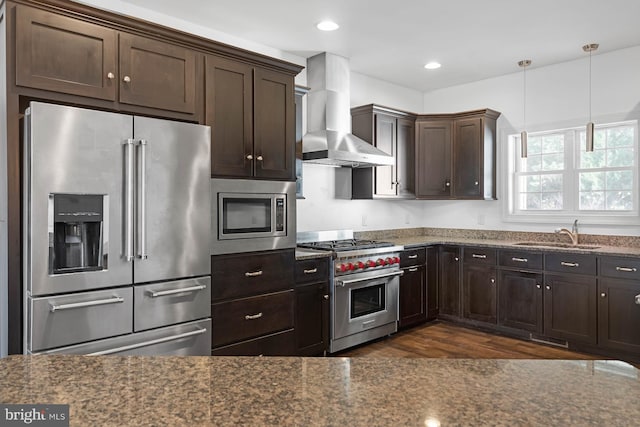 kitchen featuring wall chimney exhaust hood, dark wood-type flooring, high end appliances, sink, and decorative light fixtures