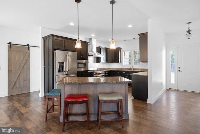 kitchen with wall chimney range hood, a barn door, decorative light fixtures, and high end appliances