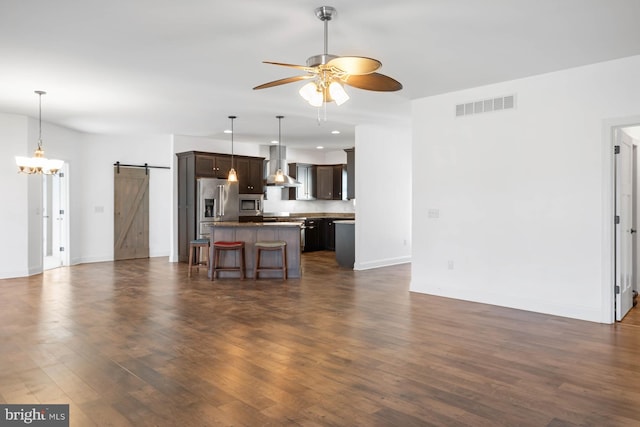 kitchen with wall chimney exhaust hood, a center island, a barn door, a kitchen bar, and appliances with stainless steel finishes