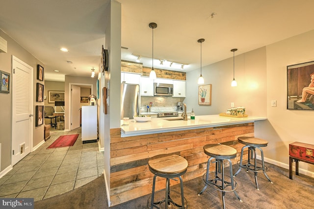 bar with backsplash, appliances with stainless steel finishes, hanging light fixtures, tile patterned flooring, and white cabinets