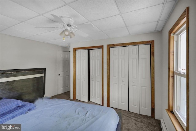 carpeted bedroom with ceiling fan, multiple closets, and a drop ceiling