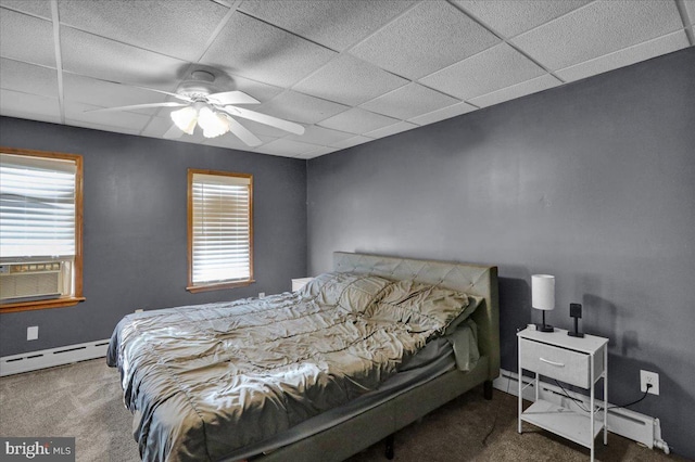 bedroom featuring ceiling fan, a baseboard heating unit, a drop ceiling, and dark colored carpet